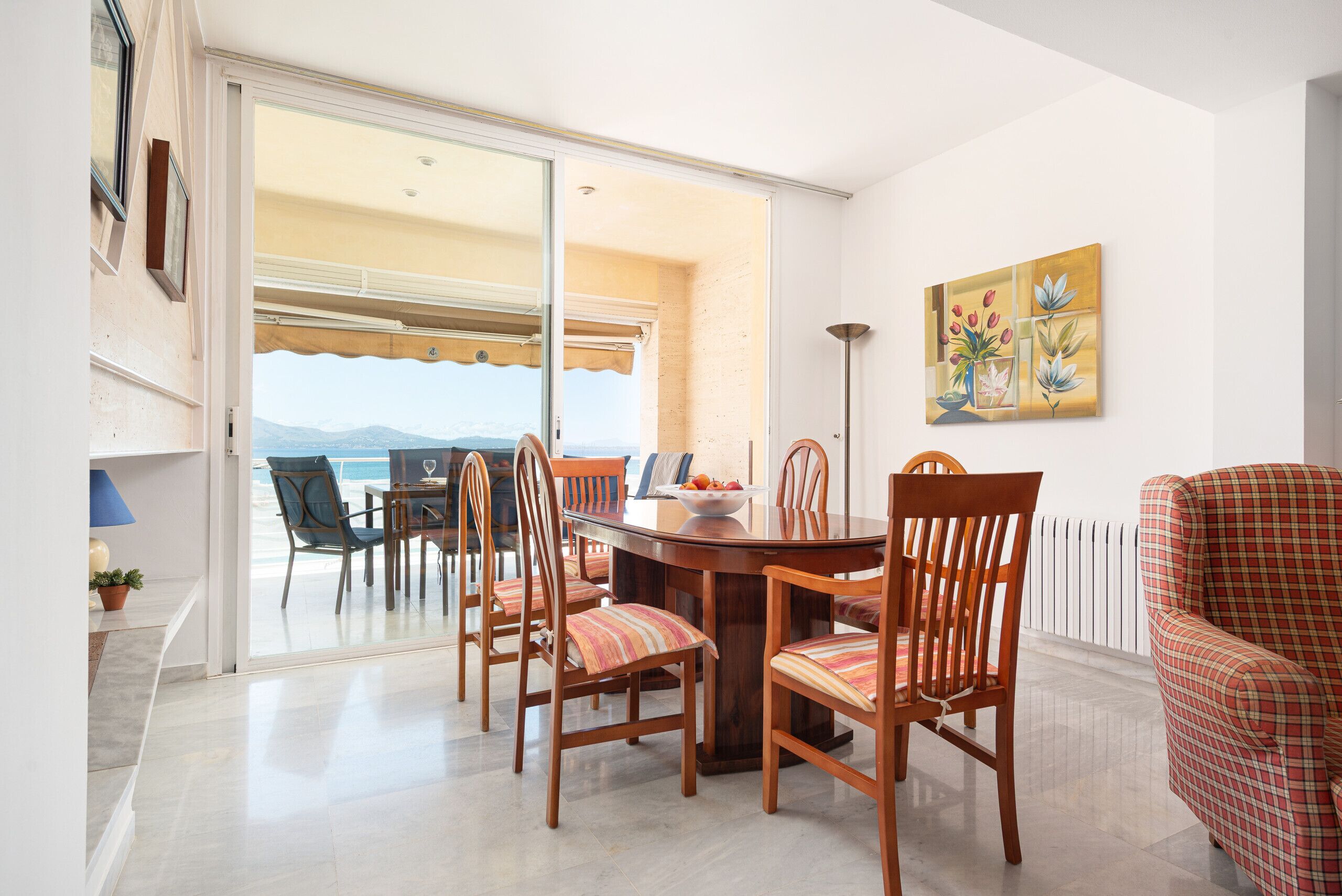 A dining area with a table and chairs, a view through a glass door, and a painting on the wall.