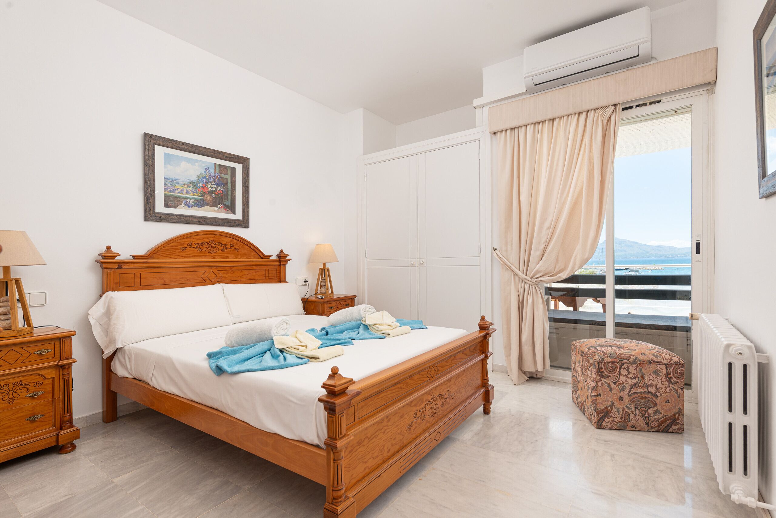 A bedroom with a wooden bed, a nightstand, a lamp, a window with curtains, and a radiator.