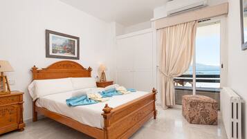 A bedroom with a wooden bed, a nightstand, a lamp, a window with curtains, and a radiator.