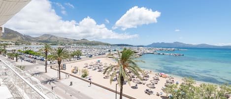 A coastal cityscape with a beach, palm trees, and a clear blue sky.