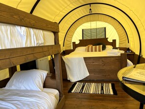 A tent-style room with bunk beds, a small table with a book, and a wooden floor. - Go Glamping in North Carolina at this Wonderful Riverside Covered Wagon in Lillington (Lillington)