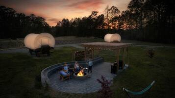 Un espacio de estar al aire libre cubierto con una chimenea, rodeado por un césped y árboles.
