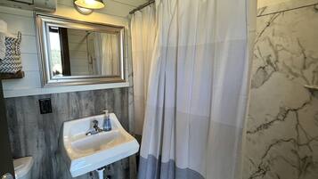A bathroom with a white sink, a mirror, a shower curtain, and a marble wall.