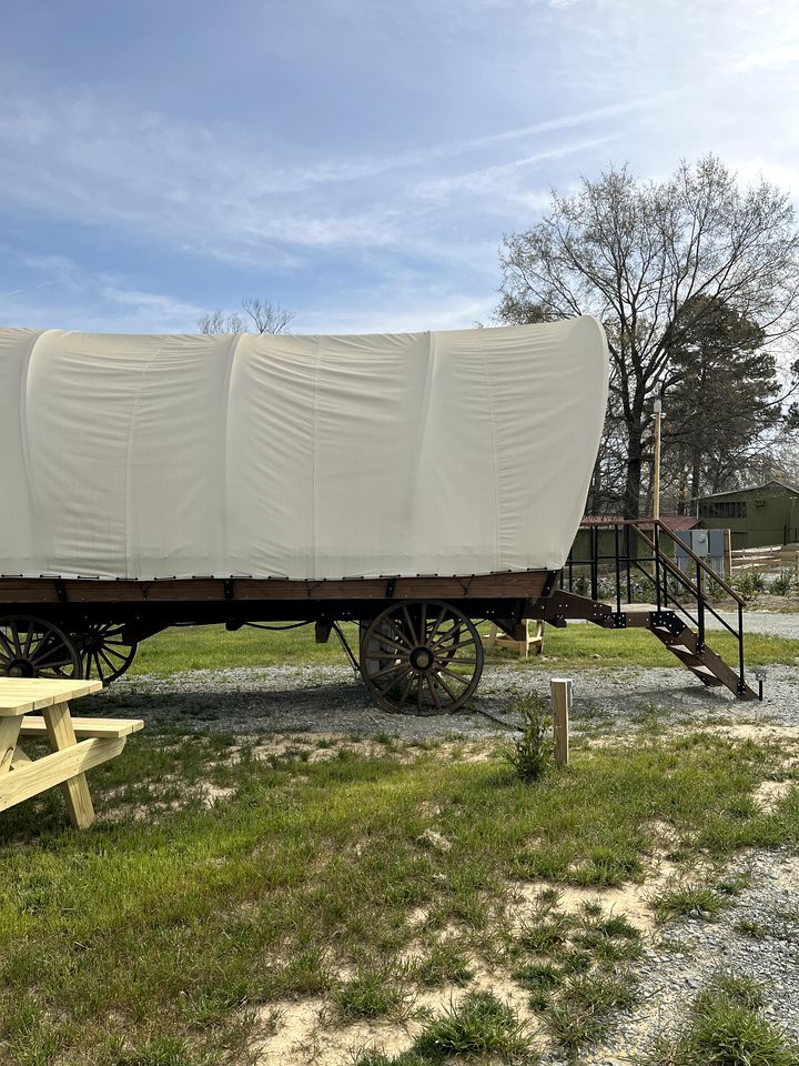 Een overdekte wagen met houten frame en wielen, een picknicktafel en een trap naar een platform.