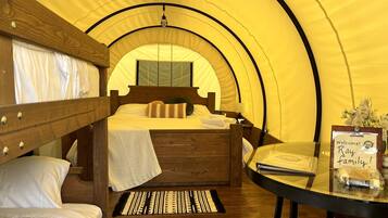 A tented accommodation room with bunk beds, a small table with a welcome sign, and a view of the tent's interior.
