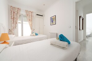 A hotel room with two beds, a radiator, a framed picture, and a door leading to another room. - Port de Pollen a Topacio 1 (Pollença)
