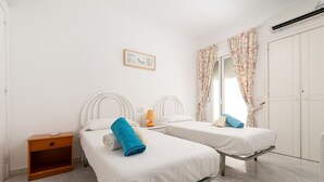 Quarto limpo e bem iluminado com duas camas de solteiro, uma mesa de cabeceira, um abajur e um guarda-roupa.