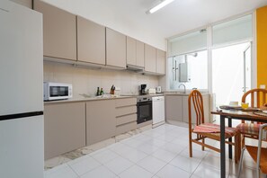 Una cocina moderna con microondas, horno y lavavajillas, una zona de comedor con mesa y sillas, y un ventanal que proporciona luz natural.