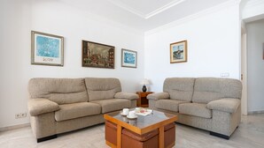 Uma sala de estar com dois sofás bege, uma mesa de centro de vidro e três obras de arte emolduradas na parede.