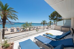 A balcony with lounge chairs, a palm tree, and a view of the beach and sea. - Port de Pollen a Topacio 1 (Pollença)