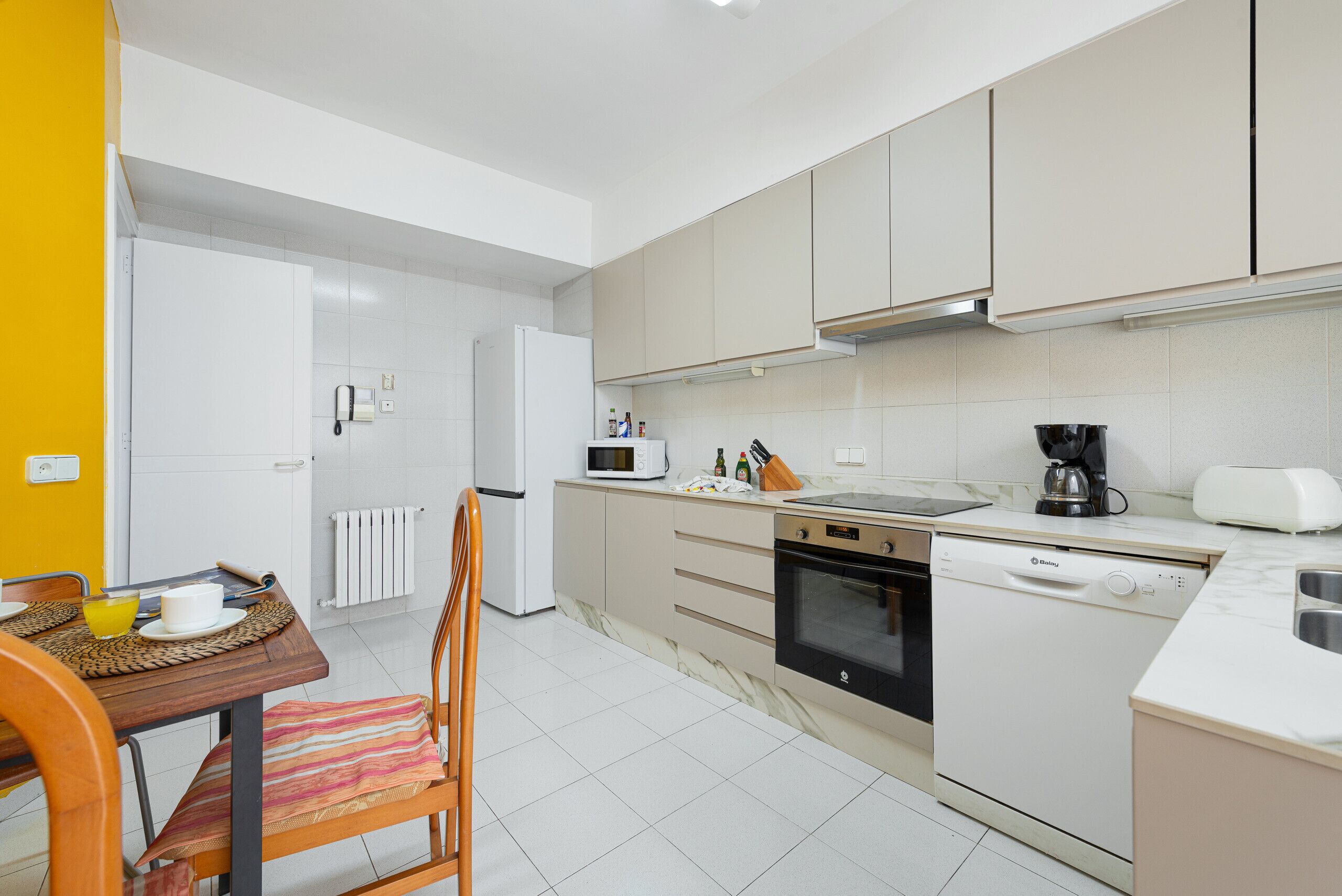 A modern kitchen with white appliances, a dining table with chairs, and a yellow wall.
