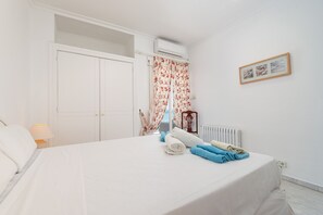 Un dormitorio con cama, un radiador, una ventana con cortinas florales, un cuadro en la pared y una puerta blanca.