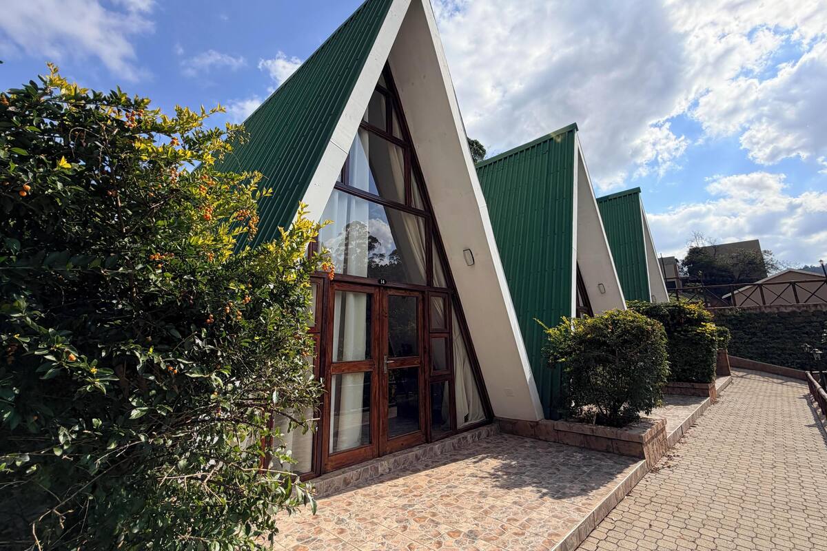 Un edificio con techo triangular, ventanas amplias y un acceso pavimentado.