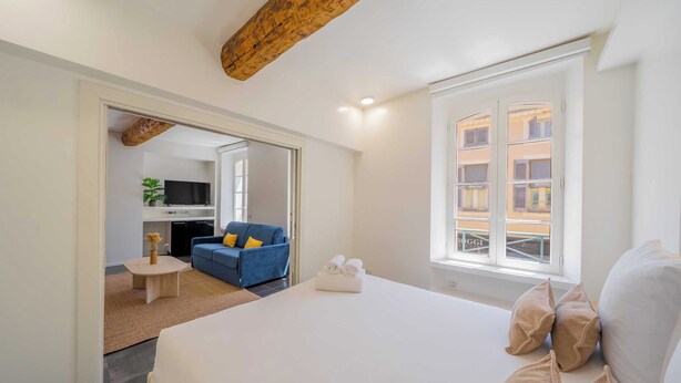 Ett modernt hotellrum med en stor säng, en soffa, en tv och utsikt över byggnader genom fönstret.
