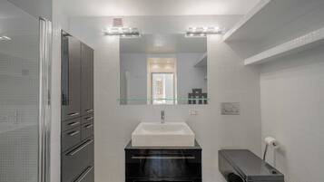 A modern bathroom with a glass shower enclosure, a white sink, and a black vanity.