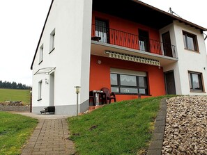 Ein zweistöckiges Gebäude mit roter Fassade, einem Balkon mit Geländer und einem gepflasterten Eingang.