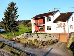Ein zweistöckiges Haus mit Balkon, einer Steinmauer und Blick auf eine grüne Landschaft.