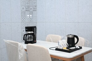 Ein Esstisch mit Kaffeemaschine, Wasserkocher und einer Serviertablett mit Tassen und Löffel.