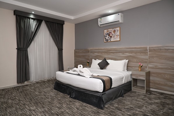 A modern hotel room with a large bed, a headboard with a wood-like finish, an air conditioning unit, and a framed artwork on the wall.