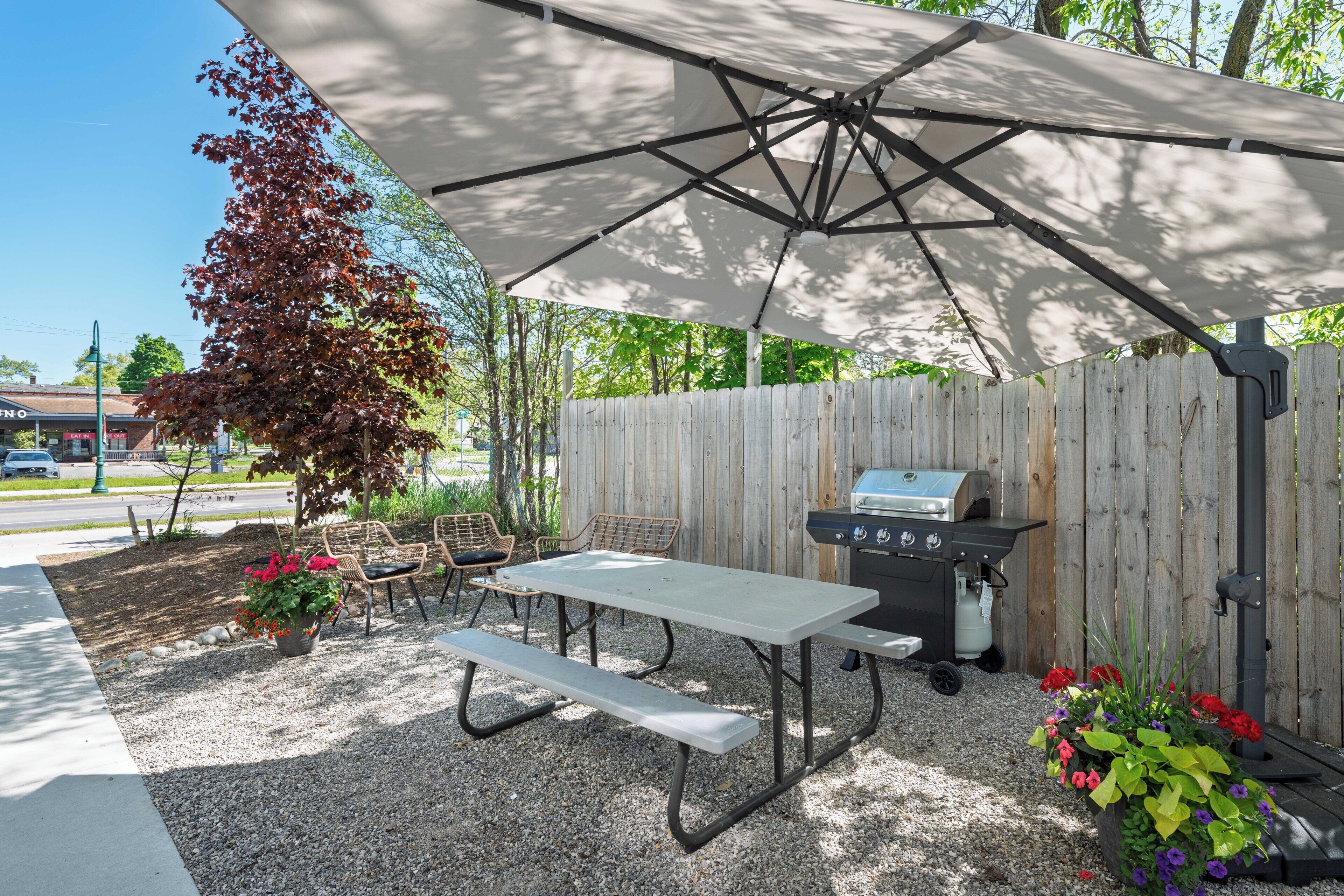 An outdoor patio with a table and benches, a grill, and a covered area.