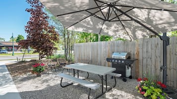An outdoor patio with a table and benches, a grill, and a covered area.