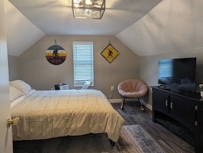 A bedroom with a bed, a chair, a TV, and a radiator. - Cave Country Creekside Getaway (Marengo)