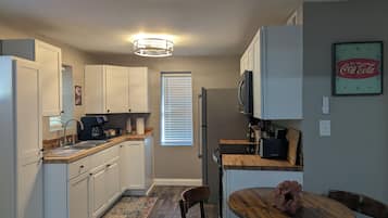 Een kleine keuken met witte kastjes, een houten aanrecht, een ingebouwde magnetron en een eethoek met een ronde tafel en twee stoelen.