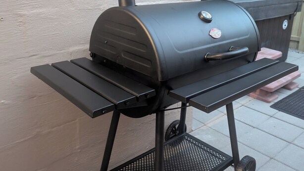 A portable barbecue grill on a metal stand with wheels, placed on a tiled patio. - Cave Country Creekside Getaway (Marengo)