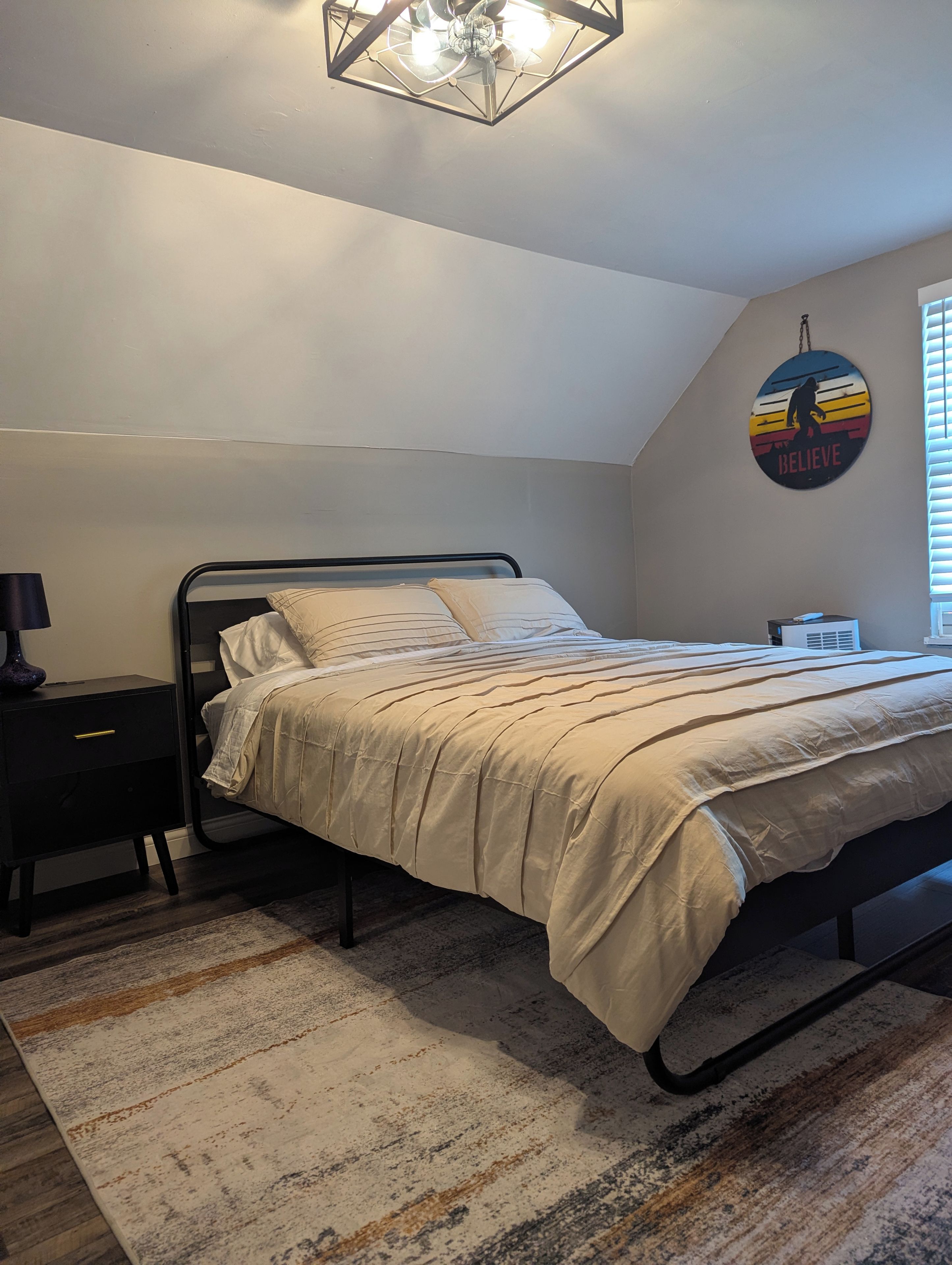 Una camera da letto con un letto, un comodino, una lampada, una sveglia a parete e un poster motivazionale.