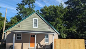 A small single-story house with a green roof, a front porch, and a wooden fence. - Cave Country Creekside Getaway (Marengo)