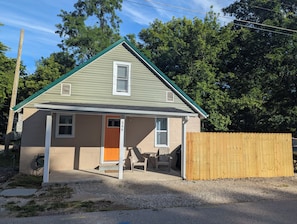 A small single-story house with a green roof, a front porch, and a wooden fence. - Cave Country Creekside Getaway (Marengo)