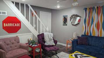 Una sala de estar con una escalera, una señal de stop roja, un sofá azul y un ventilador de techo.