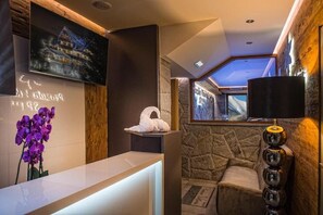 Una zona de recepció amb taulell d'informació, una escultura blanca, un televisor penjat a la paret i una paret de pedra.
