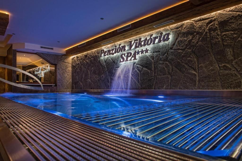 A spa area with a stone wall, a sign reading 'Pensión Viktoria SPA', and a heated pool with a waterfall feature.