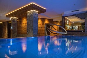 Una piscina amb fons de vidre, columnes de pedra i una escala moderna.