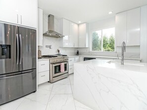 Une cuisine moderne dotée d’appareils électroménagers en acier inoxydable, de meubles blancs et d’un grand îlot central.
