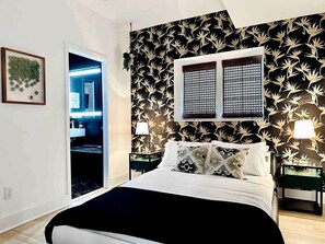 Een slaapkamer met een bed, twee nachtkastjes, een raam met jaloezieën en een deur naar een badkamer.