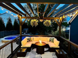Une terrasse extérieure dotée d’un foyer, de sièges confortables et de guirlandes lumineuses.