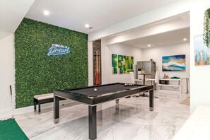 Una mesa de billar moderna en un espacio interior con pared verde y arte abstracto.