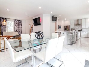 Een moderne keuken met witte kasten, een glazen eettafel en een aan de muur bevestigde televisie.