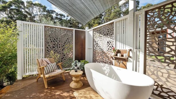 An outdoor patio with a white bathtub, a wooden chair, and a table with a bottle.