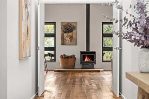 Une pièce avec un plancher en bois, une cheminée, une grande fenêtre et un tableau accroché au mur.