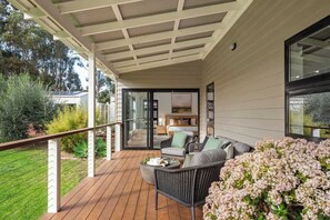 Un espace extérieur aménagé, abrité et doté d'une terrasse en bois, de meubles en osier et d'une vue sur le jardin.