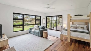 A modern bedroom with a bunk bed, a sofa, and large windows offering a view of the outdoors.