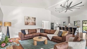 A modern living room with a sectional sofa, a round coffee table, and a dining area with a wooden table and vase.