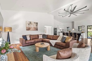 Una sala moderna con un sofá modular, una mesa de centro redonda y un comedor con mesa de madera y un florero.