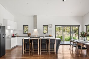 Une cuisine moderne dotée d’un îlot central, de tabourets de bar et d’un coin repas offrant une vue sur la verdure.
