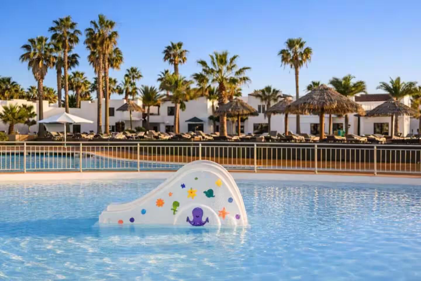 Une piscine avec un toboggan, des palmiers et des chaises longues.