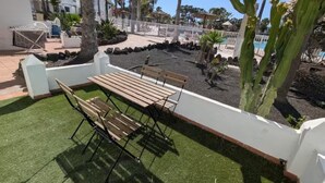 Une terrasse avec une table et des bancs, entourée d’un mur blanc, de palmiers et d’une piscine.