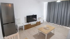 Un salon moderne avec un téléviseur à écran plat, une table basse en bois, un canapé blanc et un rideau gris.